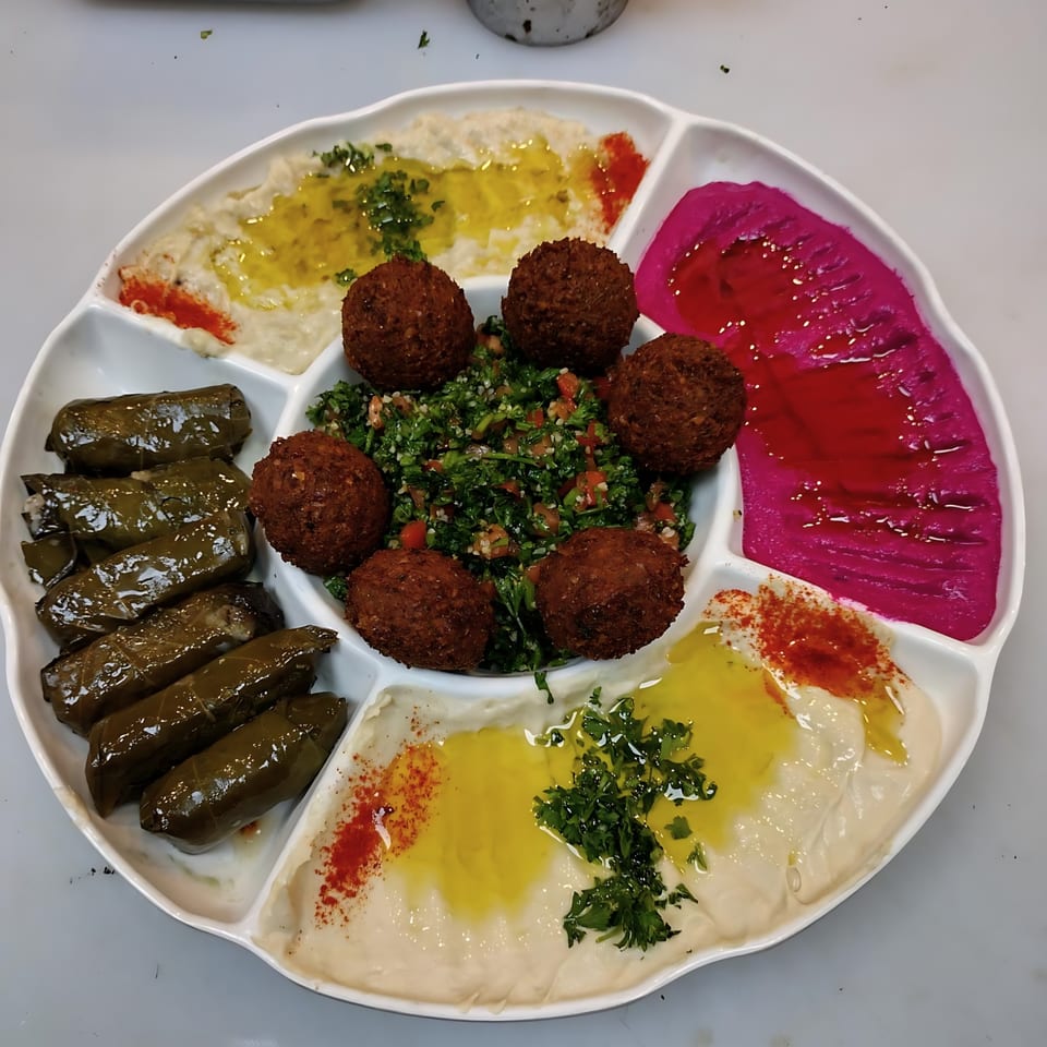 A white platter with falafel, tabbouleh, stuffed grape leaves, hummus, and a pink dip.