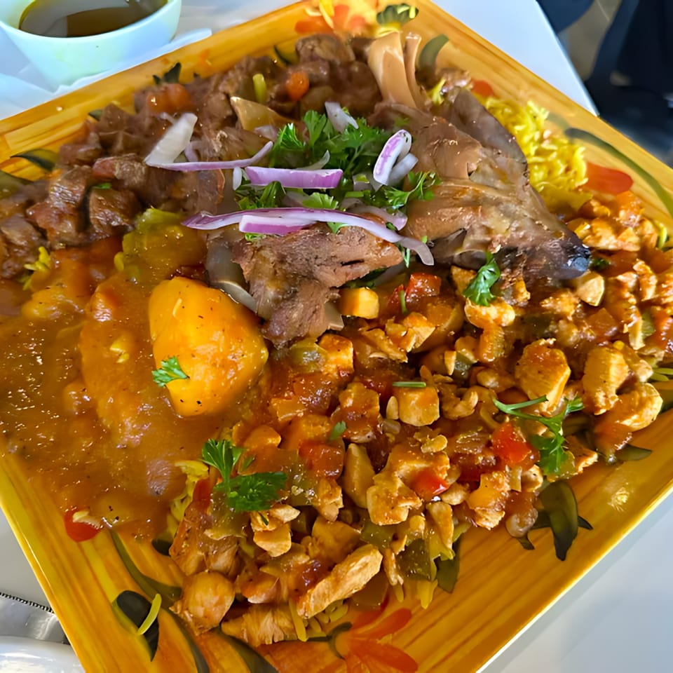 A large platter of Middle Eastern food with lamb shank, chicken, potatoes, and rice.