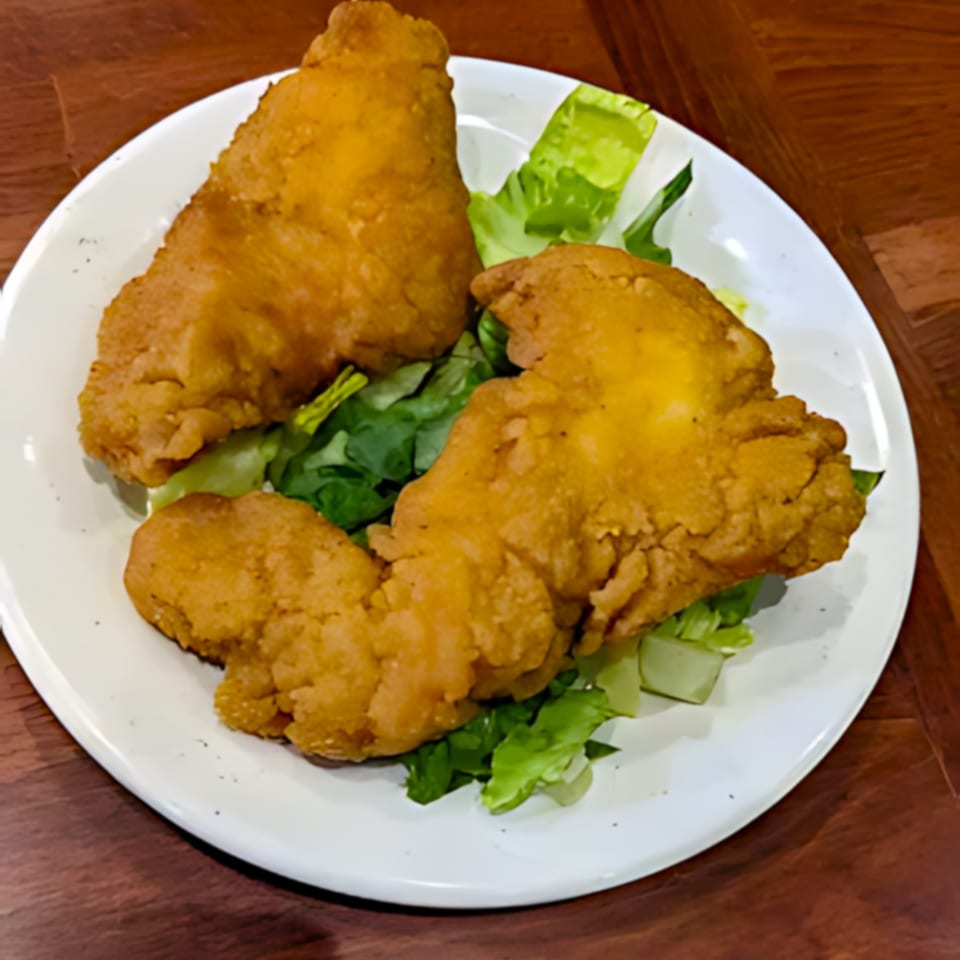 Three pieces of golden-brown fried chicken on a bed of fresh green lettuce on a white plate.