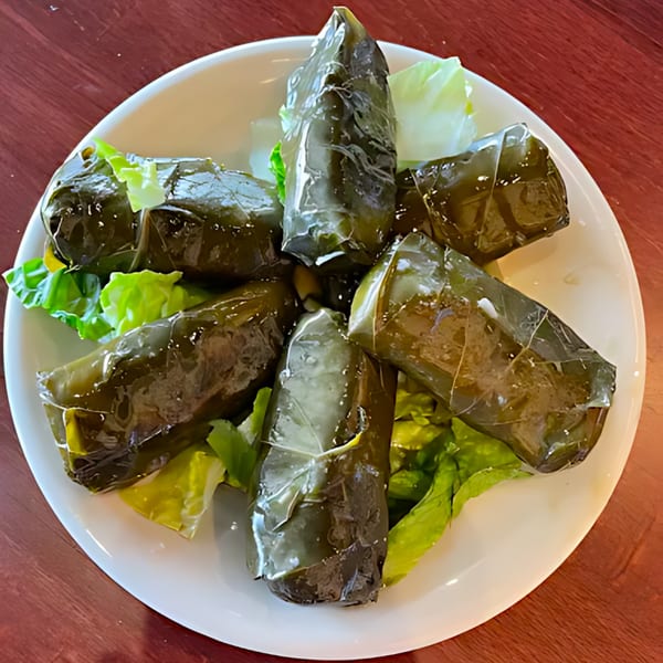 Six dolmas, or stuffed grape leaves, arranged on a bed of lettuce on a white plate.