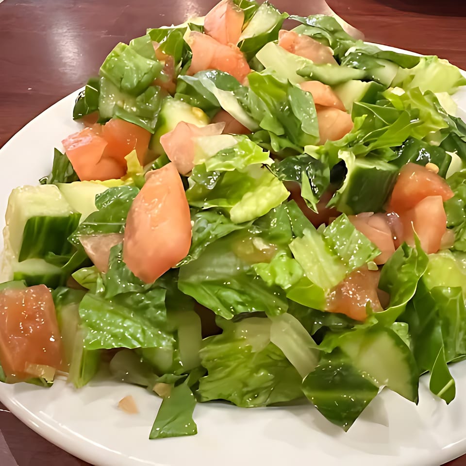 A fresh Queen of Sheba Imperial Restaurant salad with chopped lettuce, tomatoes, and cucumbers.