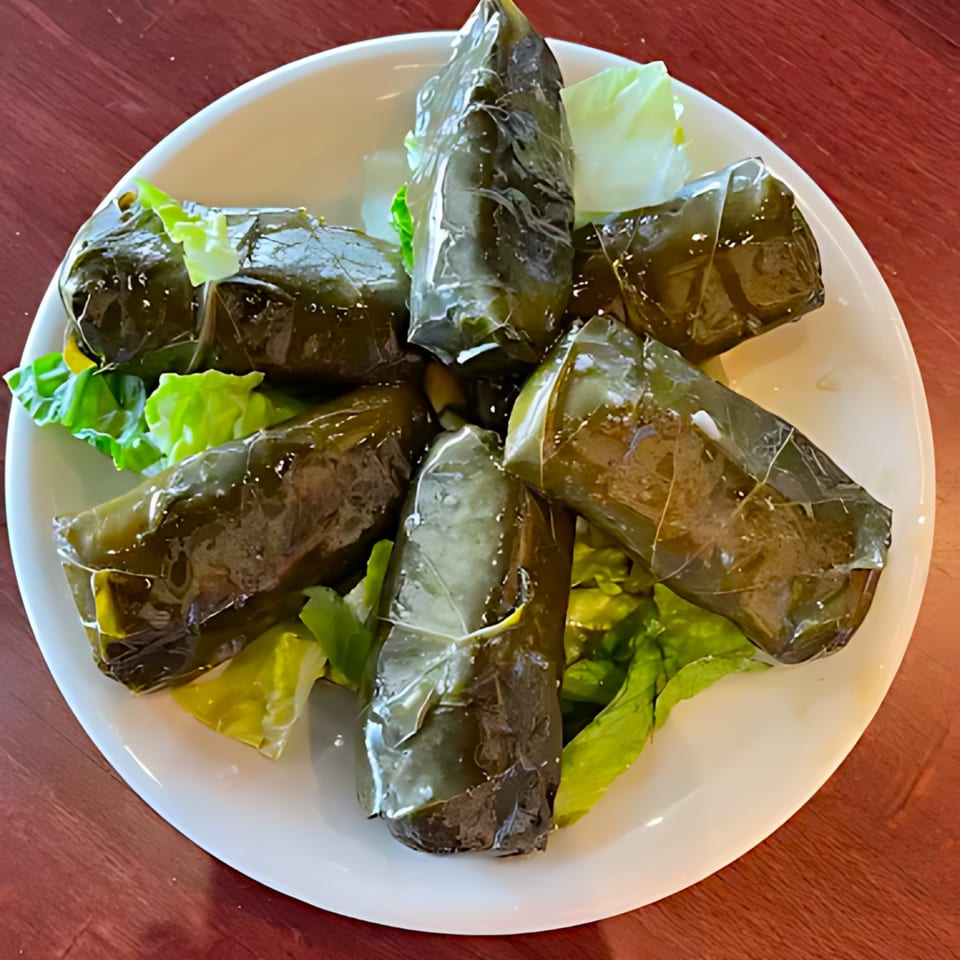 Six dolmas, or stuffed grape leaves, arranged on a bed of fresh lettuce on a white plate.