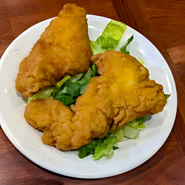 Two pieces of golden-brown fried fish on a bed of fresh green lettuce on a white plate.