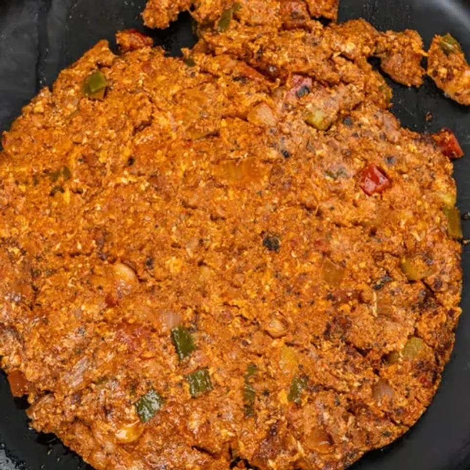Close-up of a round, orange-red Middle Eastern dish with visible vegetables on a black plate.