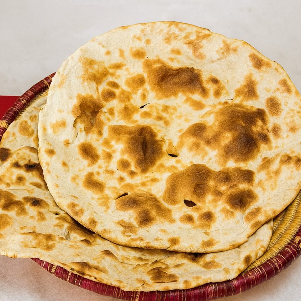 Two round, golden-brown flatbreads with dark spots, served in a red and gold woven basket.
