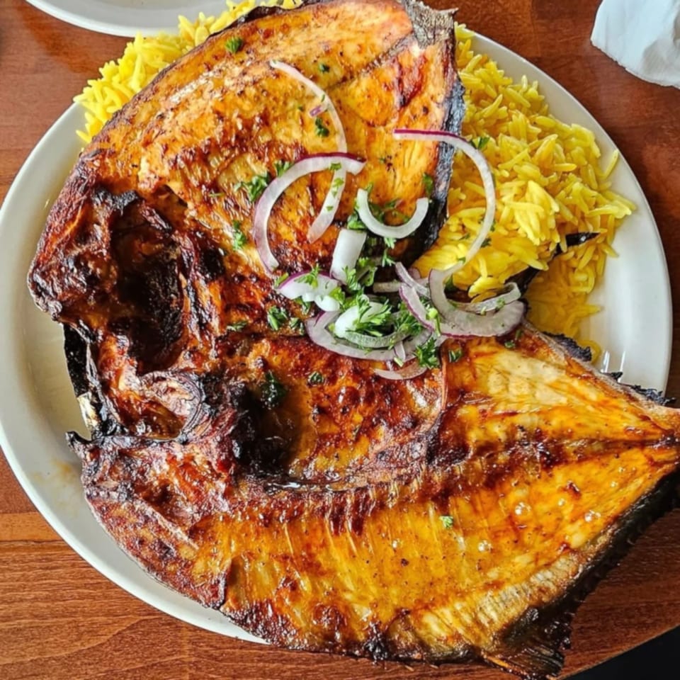 Grilled whole fish with crispy skin, topped with onions and parsley, served with yellow rice.