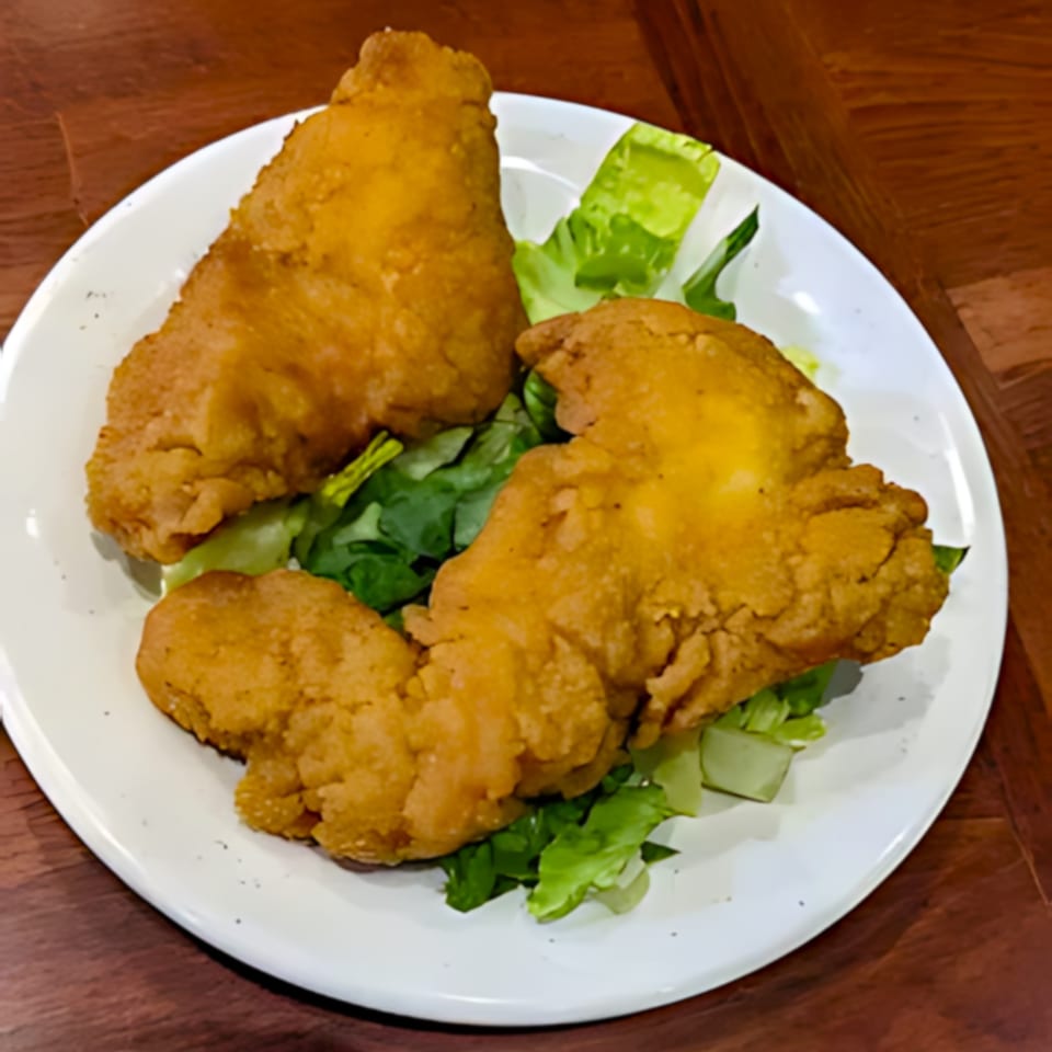 Two pieces of golden-brown fried fish on a bed of fresh green lettuce on a white plate.