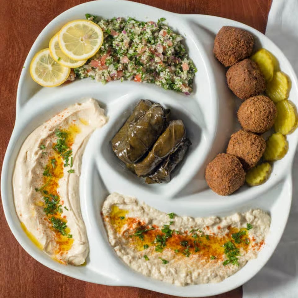 A white platter with falafel, hummus, baba ghanoush, tabbouleh, and stuffed grape leaves.