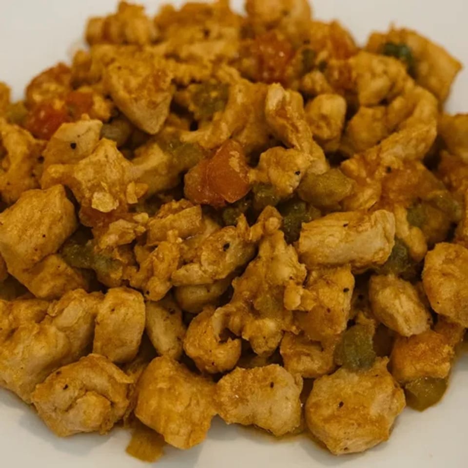Close-up of golden-brown chicken pieces mixed with green and red vegetables on a white plate.